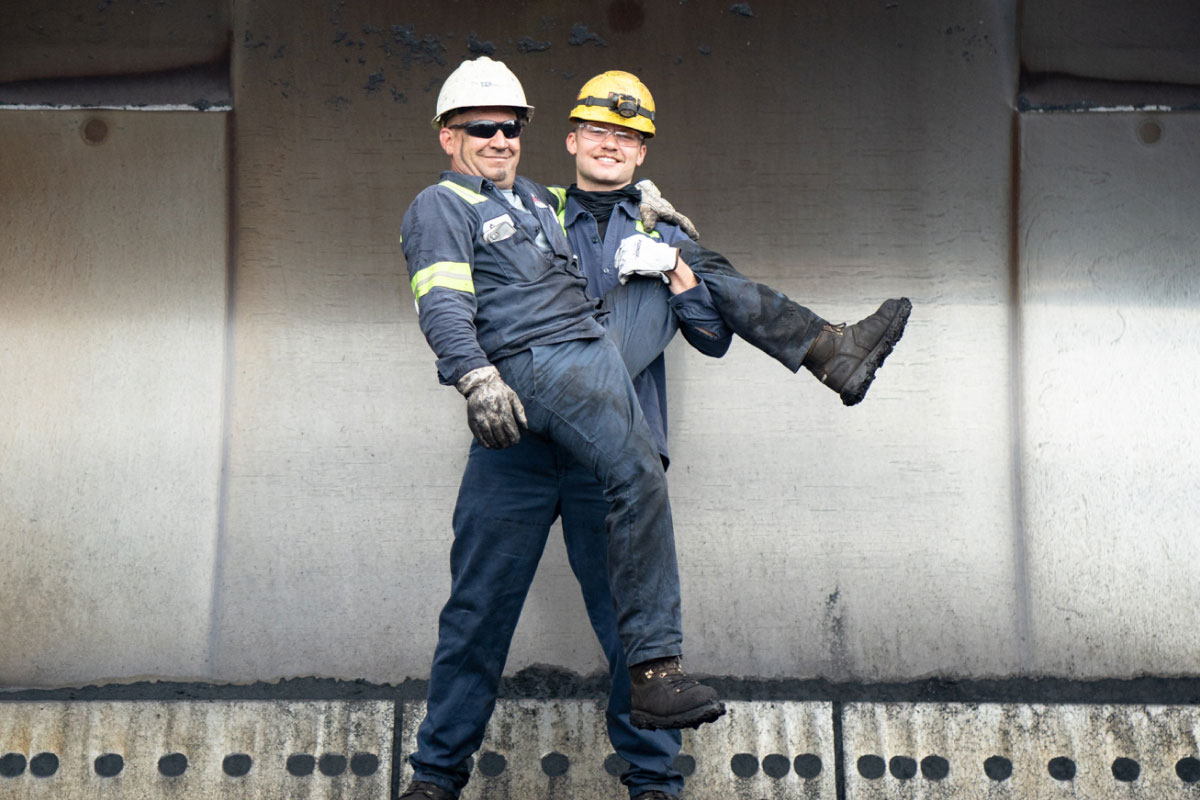 Bulk Team Member Carrying Fellow Member Both Wearing PPE