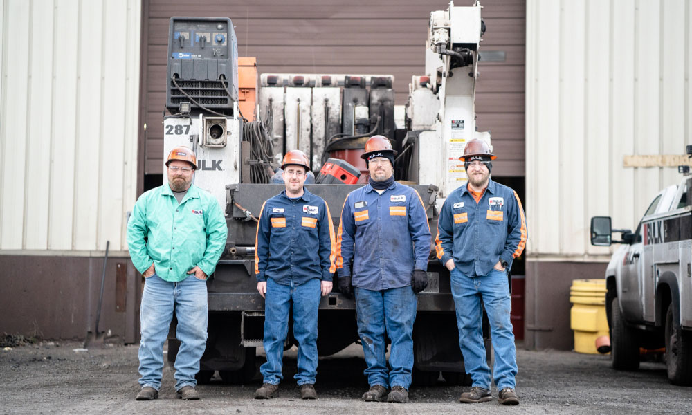 BULK Team Wearing Hard Hats & Safety Glasses Standing in Front of Heavy Equipment